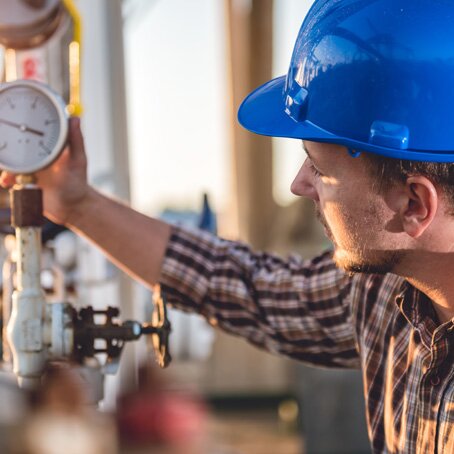 man in blue safety helmet reading meters on pipes