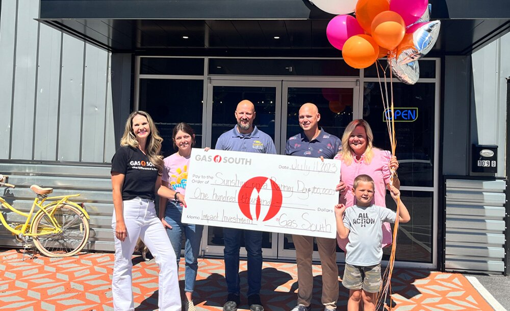 people surrounding a large donation check outside of a nonprofit organization 