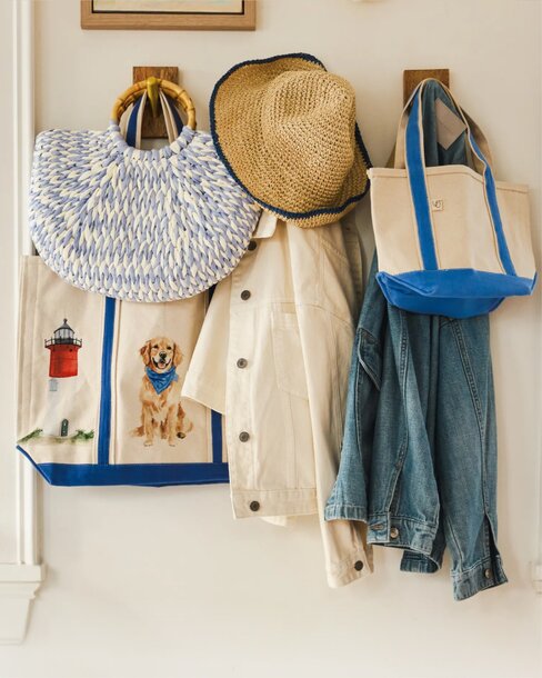 A collection of woven tote bags, a straw sun hat, a light jacket, and a denim shirt hanging on wall hooks, styled for summer outings.