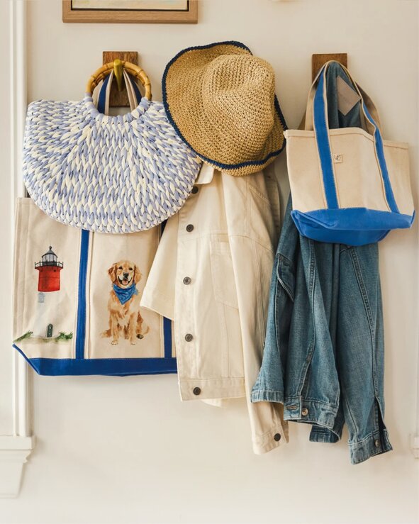 A collection of woven tote bags, a straw sun hat, a light jacket, and a denim shirt hanging on wall hooks, styled for summer outings.