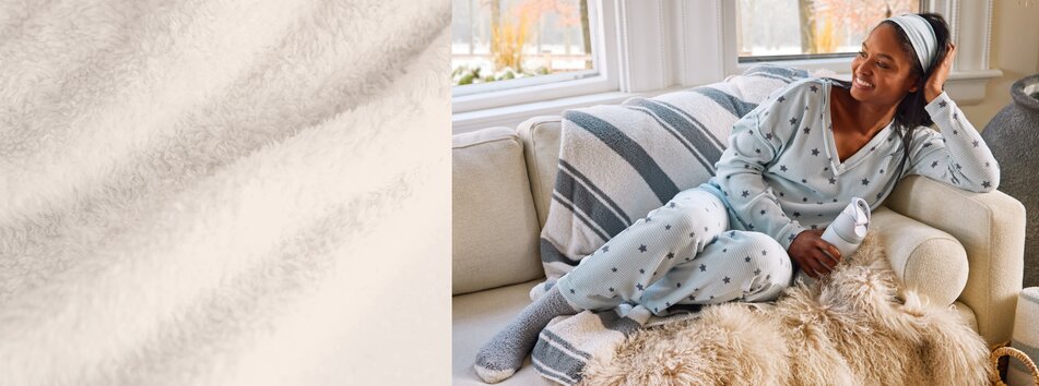 Model lounging on the couch wearing set of pajamas with star motif and fuzzy socks, holding an Owala water bottle