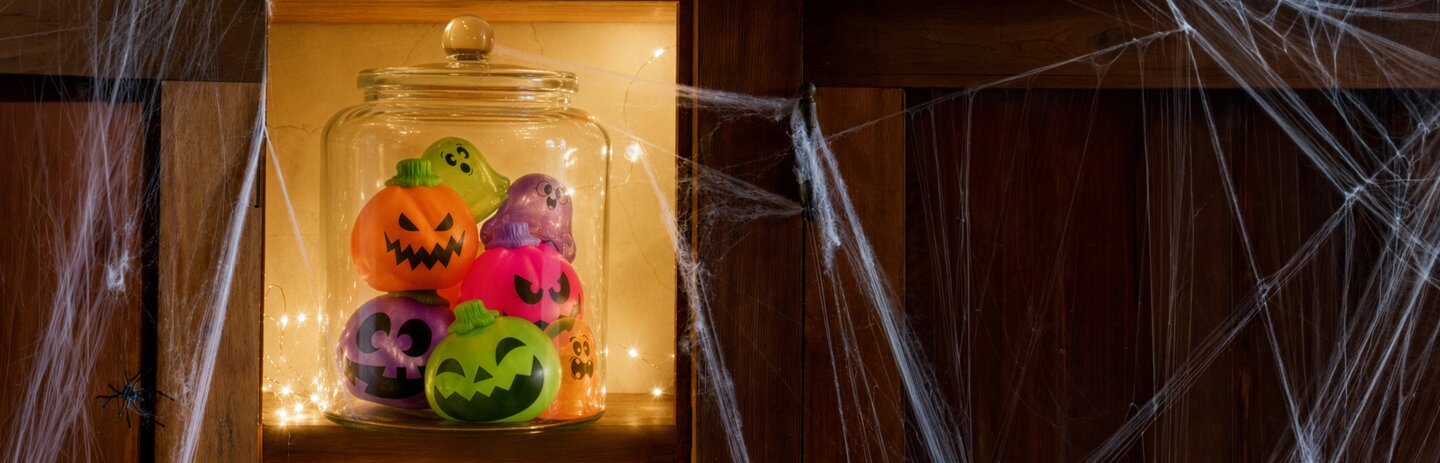 Halloween NeeDoh squishies displayed in a glowing glass jar surrounded by spiderwebs.