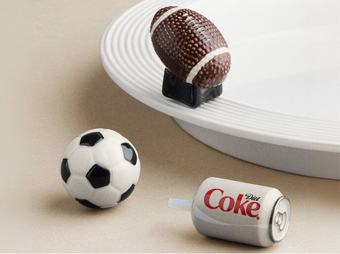 Football, soccer ball, and Diet Coke Nora Fleming mini ornaments displayed on a white serving tray