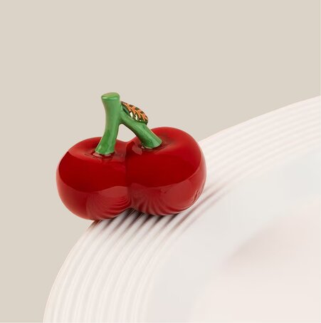 Nora Fleming Cherries mini ornament attached to the rim of a white serving bowl.