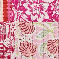 Close up of patchwork-style floral textile with pink, blush, and cream tones, featuring hand-block–style flowers, leafy motifs, and vertical stitched quilting lines.