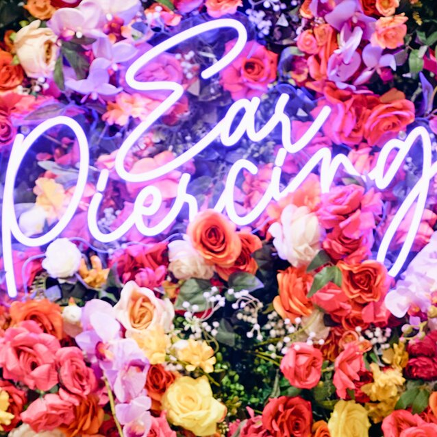 Colorful floral wall with a glowing neon “Ear Piercing” sign.