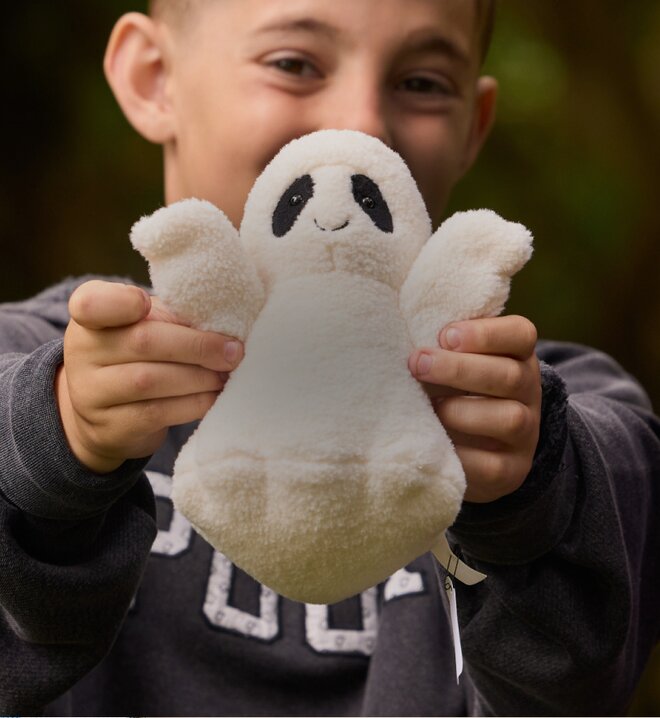 Child holding up a soft white Jellycat ghost plush toy outdoors.