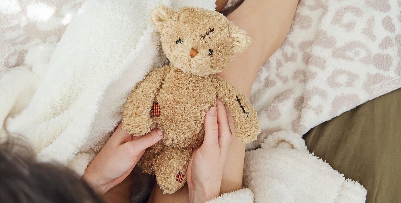 Image of a model holding a Bukowski bear in a cozy robe and blankets