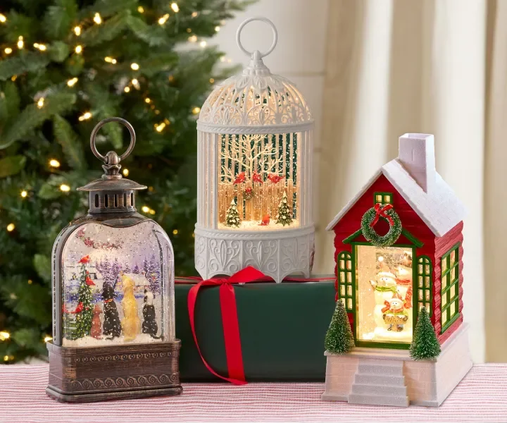 Image of three Christmas lanterns displayed in front of a lit up Christmas tree