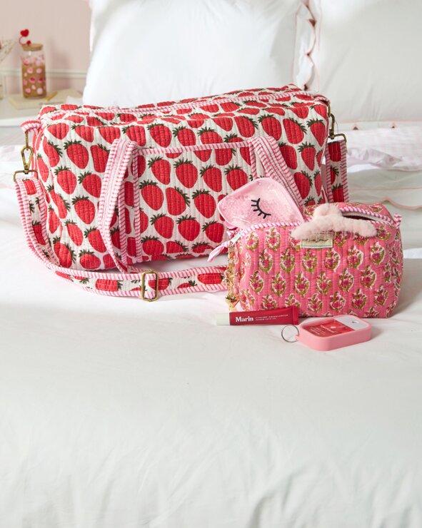 Image of red, pink and white block print Strawflower duffel bag and cosmetic bag on a bed.