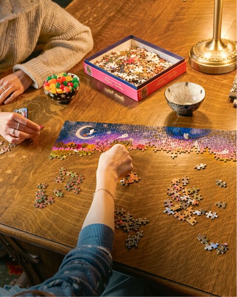 Family working on a jigsaw puzzle around a table. Shop toys and games.