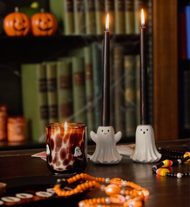 Halloween display featuring two ghost-shaped candleholders, a glowing ghost-patterned candle, and orange and black beaded decorations.