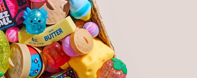Basket overflowing with colorful squishies and sensory toys on a light neutral background.