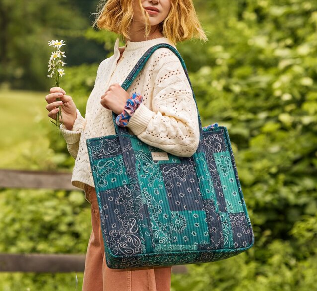 Woman outdoors carrying a Strawflower blue and teal patchwork bandana-print tote bag.