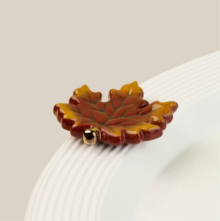 Nora Fleming autumn maple leaf mini ornament attached to the rim of a white serving bowl.