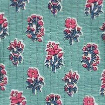 Close up of teal quilted textile with repeating hand-block–style floral motifs in pink and indigo, accented by vertical stitched lines and pink-and-white striped trim.