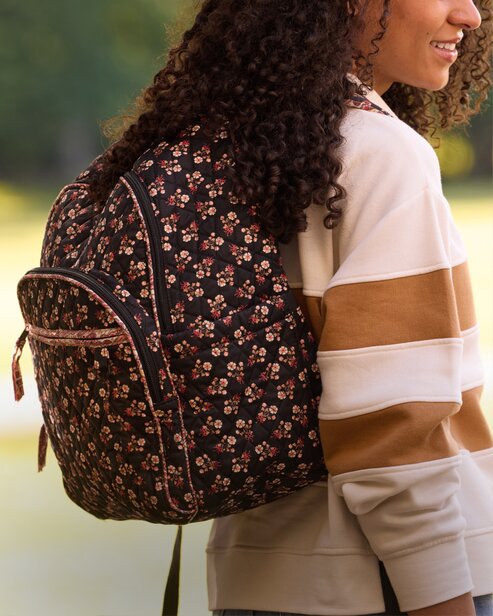 Person wearing a floral Vera Bradley backpack over a colorblock sweatshirt outdoors.