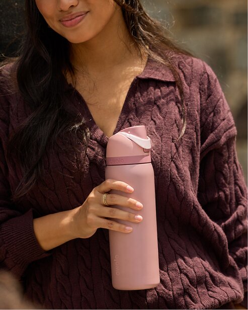 Woman holding a pink Owala water bottle while wearing a burgundy sweater.