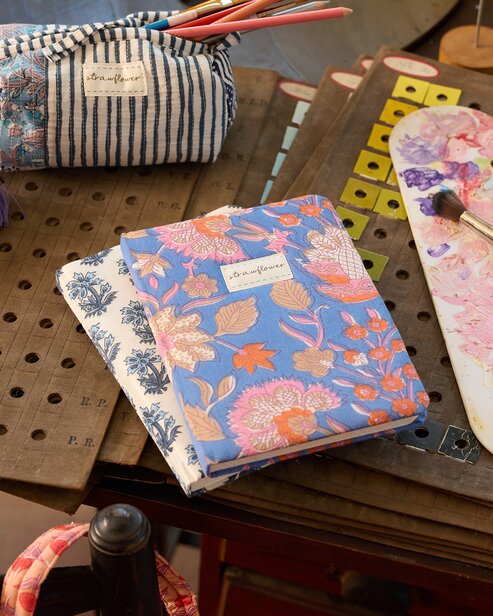 Floral Strawflower notebooks and a striped pencil pouch arranged with art supplies on a craft table.