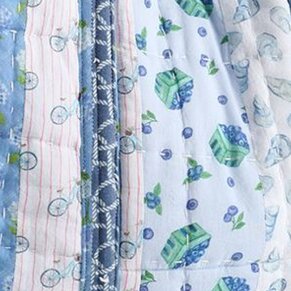 Close-up of a blue-toned patchwork fabric with mixed patterns including stripes, berries, and geometric designs, stitched together with visible seams.