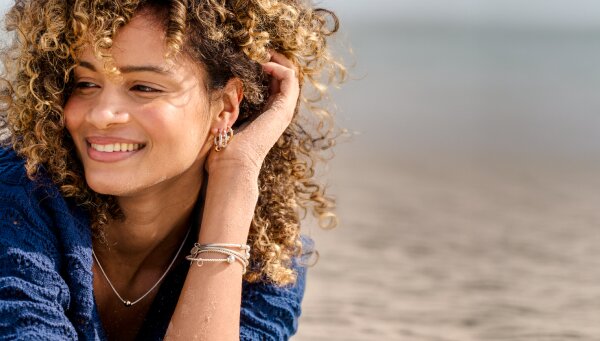 Woman wearing Cape Cod Jewelry bracelets, earrings, and necklace while relaxing on a beach.