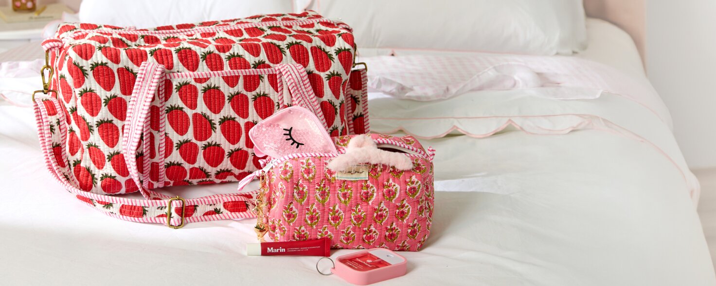 Image of red, pink and white block print Strawflower duffel bag and cosmetic bag on a bed.