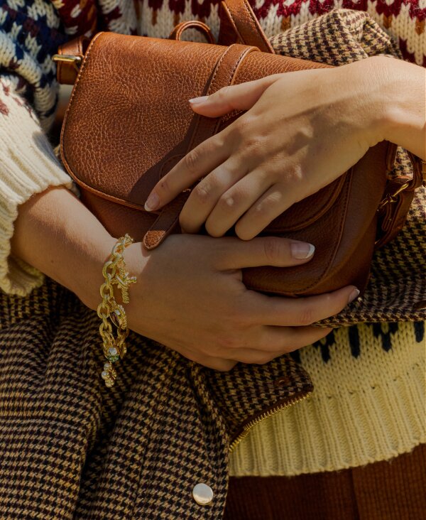 Person in a patterned sweater holding a brown handbag beside a car.