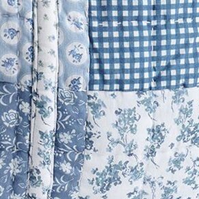 Close-up of coordinated blue fabrics including gingham checks and intricate floral patterns in soft blue and white tones, arranged in layered swatches.