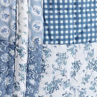 Close-up of coordinated blue fabrics including gingham checks and intricate floral patterns in soft blue and white tones, arranged in layered swatches.