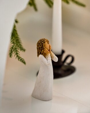 Willow Tree angel figurine in a white dress with gold accents, standing beneath festive greenery.