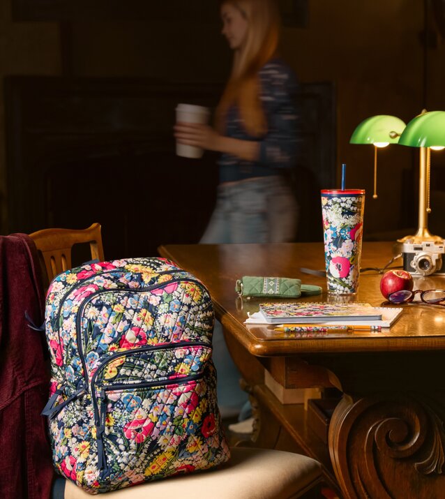 Floral Vera Bradley backpack and school essentials on a library table—get 25% off in store and online. Shop Vera Bradley.