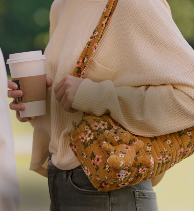 Person carrying a floral crossbody bag while holding a coffee cup.