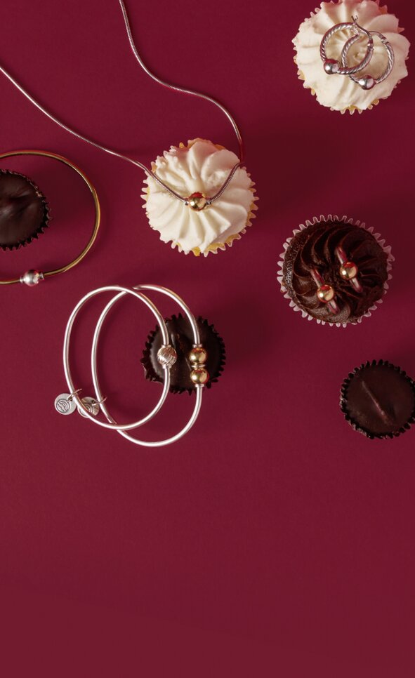 Image of Cape Cod Jewelry pieces on a berry colored backdrop among valentine's day candies and cupcakes. featuring the classic Cape Cod single, double and triple ball bracelets, single ball necklace, and single ball earrings.