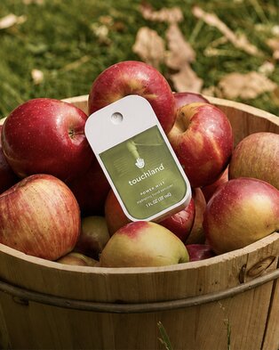 Touchland hand sanitizer displayed in a basket of fresh apples outdoors.
