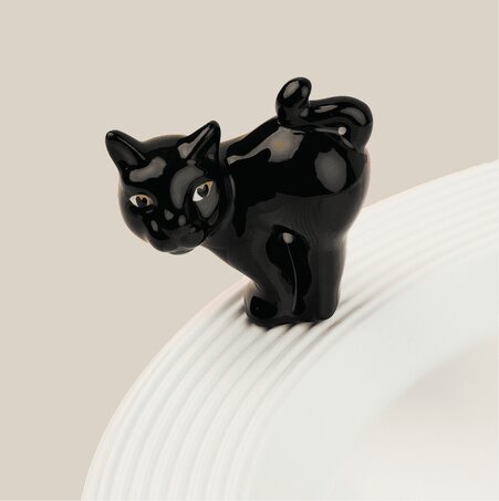 Nora Fleming Halloween black cat mini ornament perched on the rim of a white serving bowl.