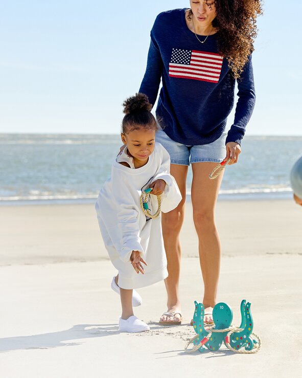 An adult and child playing together on the beach with sand toys near the shoreline on a sunny day.