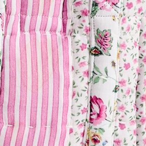 Close-up of mixed pink fabrics featuring soft vertical stripes alongside delicate floral prints in shades of blush, rose, and green on a light background.