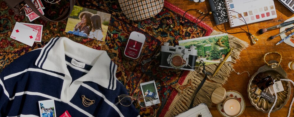 Flat lay of fall-inspired fashion, photos, camera, jewelry, candle, and stationery arranged on a patterned rug and wood table.