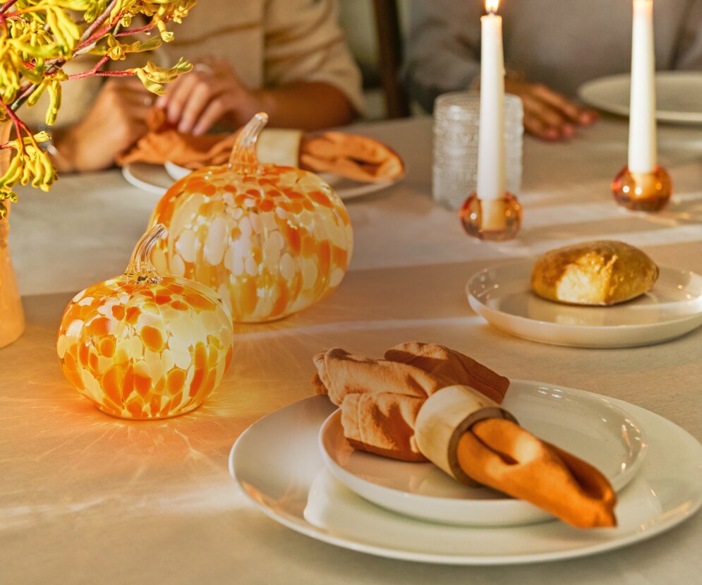 Autumn dining table set with confetti glass pumpkins, candles, and place settings for a cozy seasonal meal.
