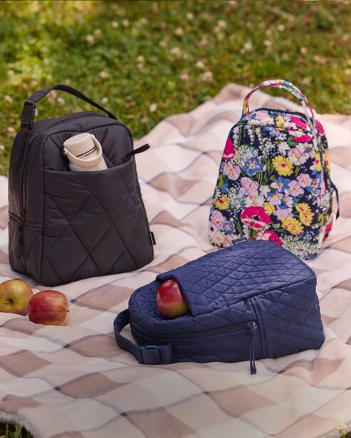 Vera Bradley quilted lunch bags and a floral backpack arranged on a picnic blanket with apples.