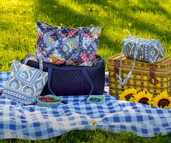 Person wearing a cream American flag sweater and carrying a navy Vera Bradley  quilted tote bag in front of a hanging American flag outdoors.