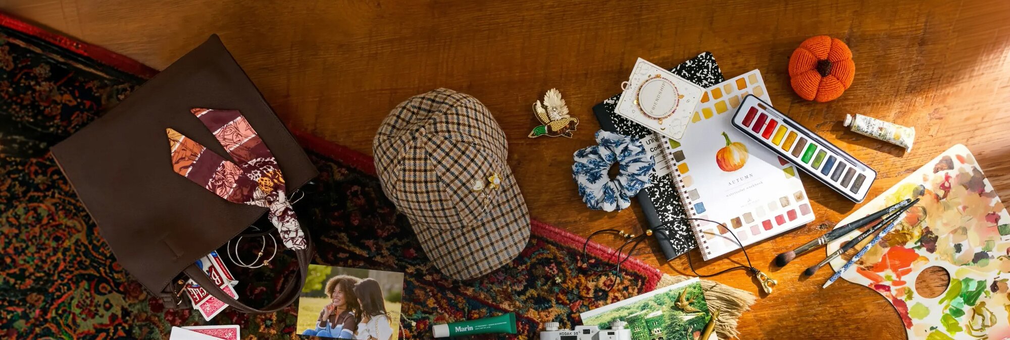 Flat lay of fall-inspired fashion, photos, camera, jewelry, candle, and stationery arranged on a patterned rug and wood table.