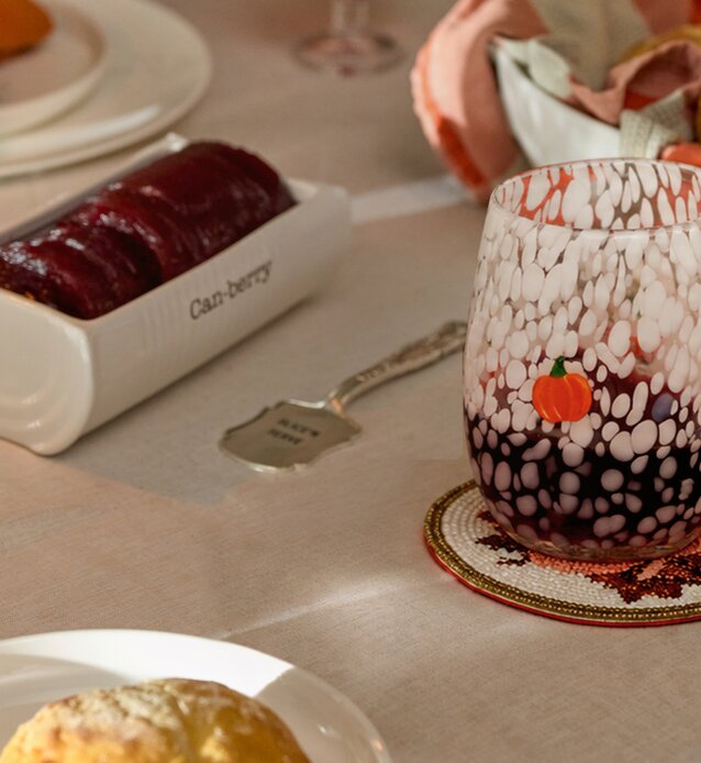 Pumpkin-speckled glass beside a cranberry serving dish on a fall table setting.