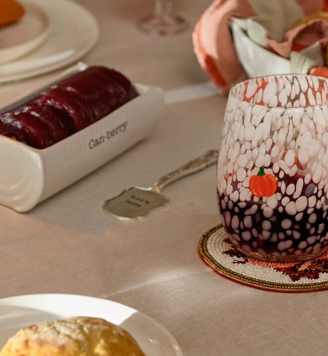 Pumpkin-speckled glass beside a cranberry serving dish on a fall table setting.