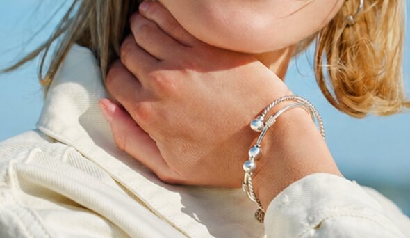 Person wearing layered silver Cape Cod–style bracelets outdoors.