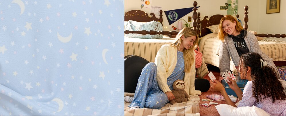 Three friends in pajamas relaxing and playing cards together in a cozy dorm room, beside a close-up of blue moon-and-star fabric.