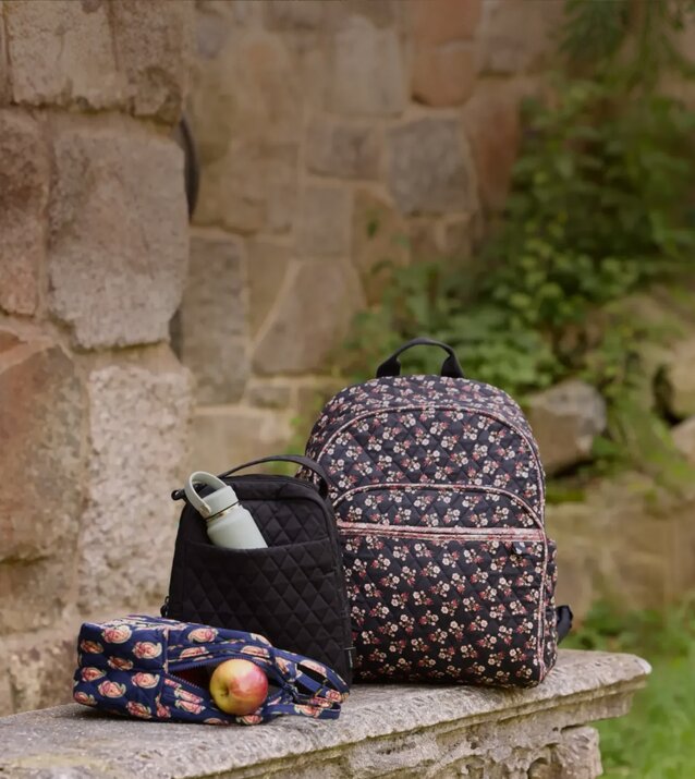 Floral Vera Bradley backpack and school essentials on a library table—get 25% off in store and online. Shop Vera Bradley.