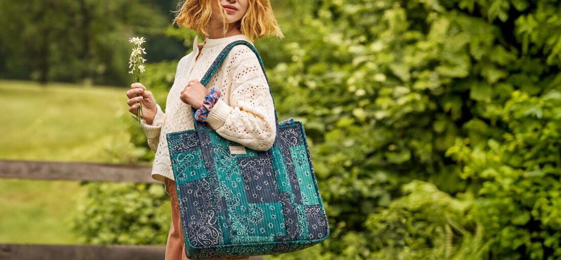 Woman outdoors carrying a Strawflower blue and teal patchwork bandana-print tote bag.