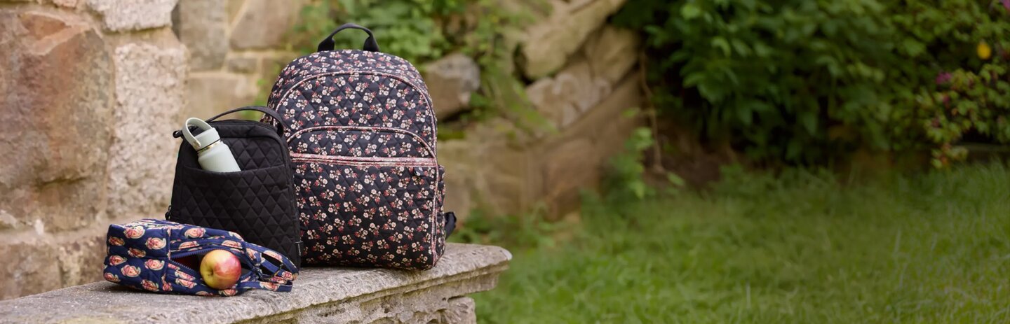 Floral Vera Bradley backpack and school essentials on a library table—get 25% off in store and online. Shop Vera Bradley.