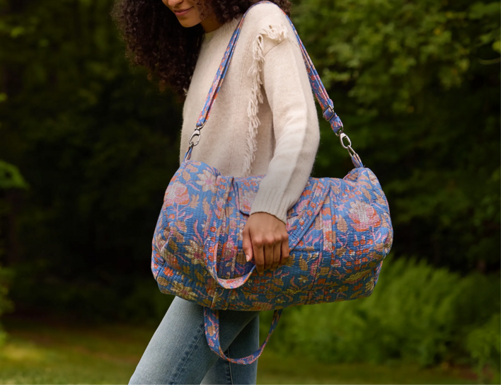 Woman outdoors carrying a Strawflower blue floral quilted duffel bag.